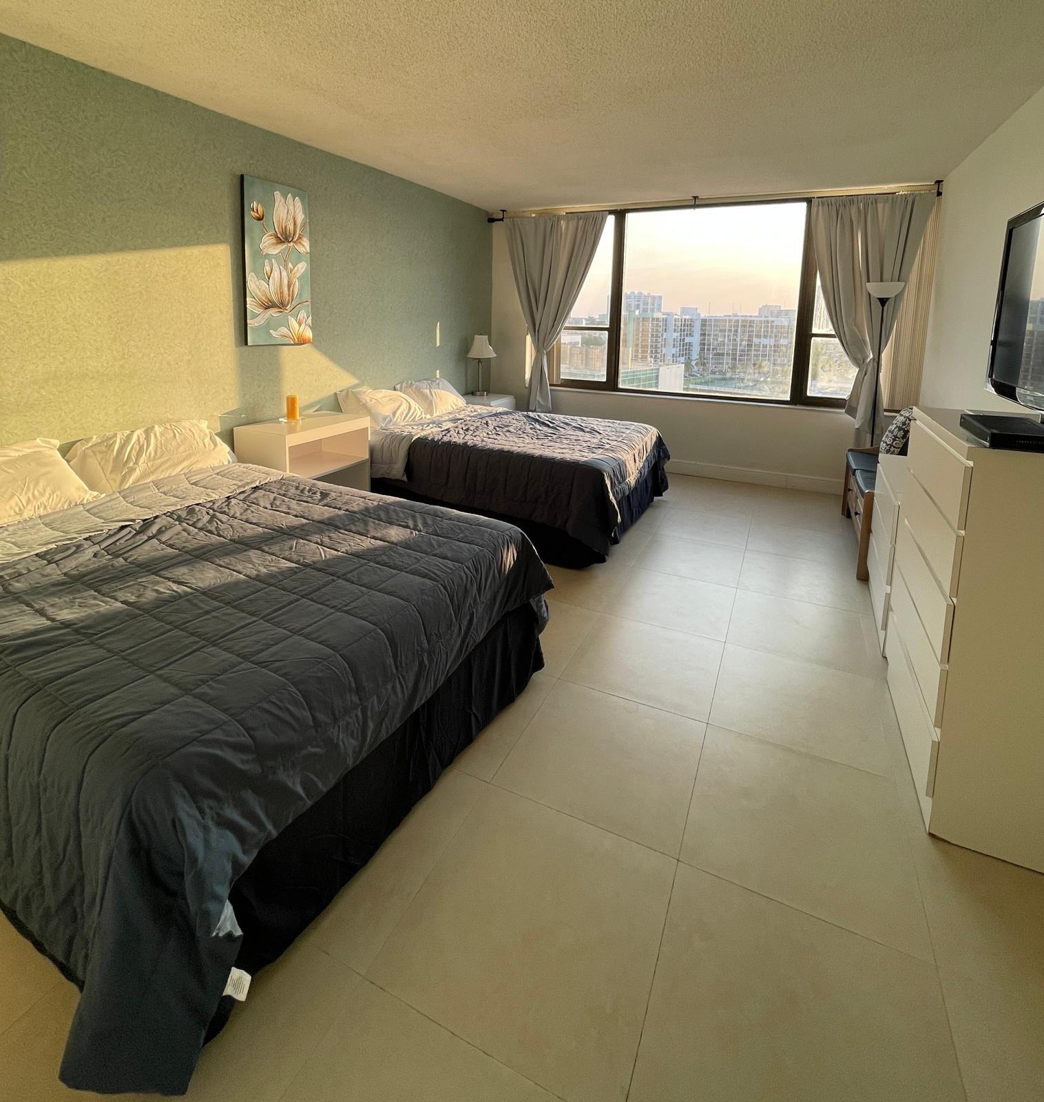 Primary bedroom with two plush beds, soft green walls and a wide window with water views