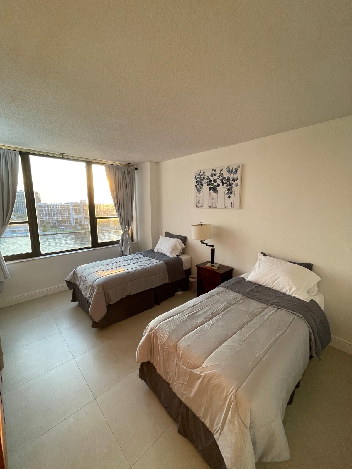 Second bedroom with two neatly made beds and a wide window facing the Intracoastal at dusk