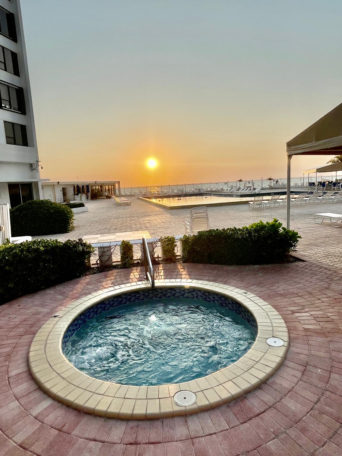 Bubbling round hot tub on the pool deck with the ocean and sunset beyond