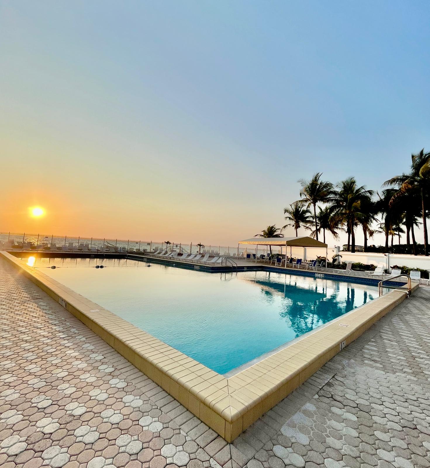 Large oceanfront pool at sunset framed by palm trees, ocean on the horizon